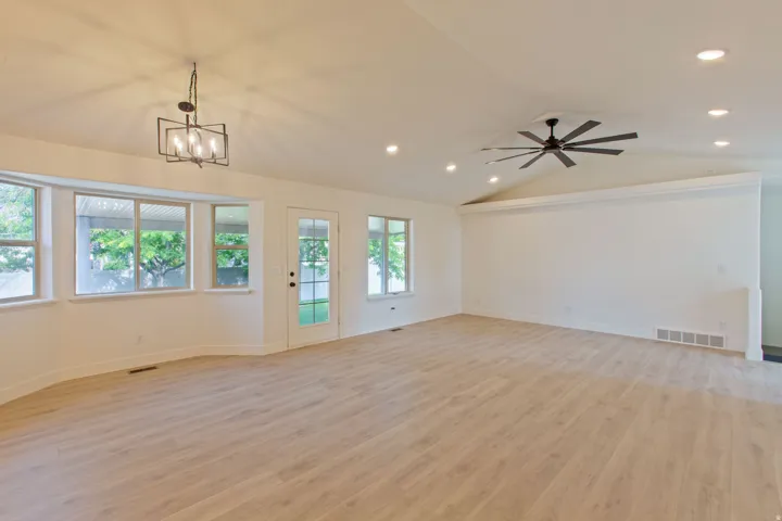 Spacious room featuring wood-finish flooring, a vaulted ceiling with a modern ceiling fan, recessed lighting, and a bay window