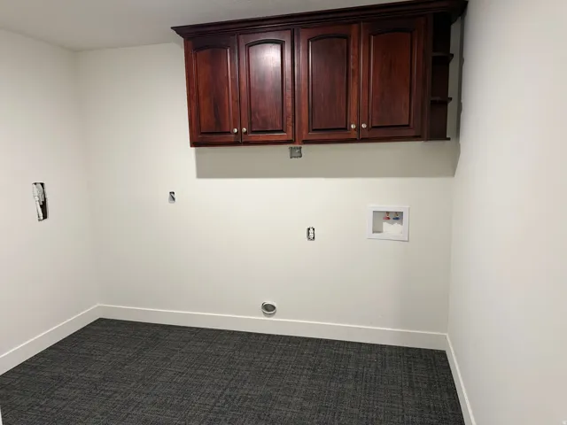Laundry area featuring dark wood-finish cabinetry with silver-tone hardware, a laundry hookup box, a dryer vent, and patterned gray carpet