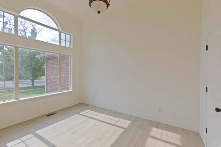Room featuring a large arched window with transom detailing, wood-finish flooring, crown molding, and a ceiling-mounted light fixture