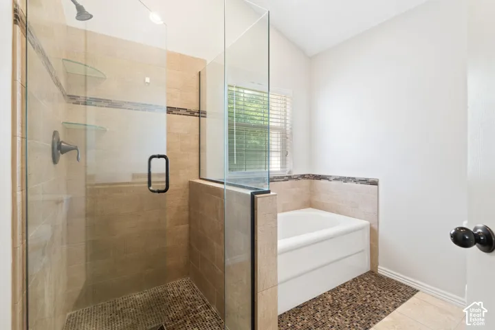 Bathroom featuring a glass-enclosed shower with tiled walls and two glass shelves, a white soaking tub, and a window with blinds