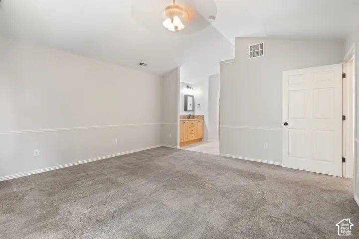 Spacious room featuring vaulted ceilings, a ceiling fan with integrated lighting, and a neutral carpeted floor
