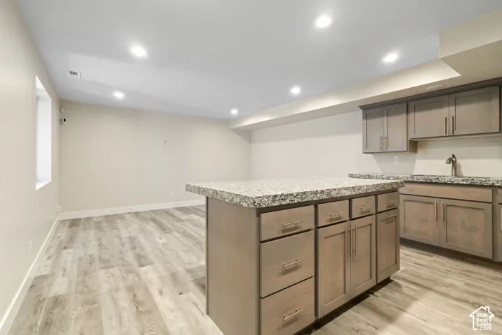 Kitchenette featuring an island with granite countertops, wood-finish cabinetry, and recessed lighting