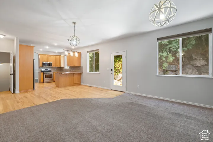 Open-concept living area with mixed flooring, featuring a kitchen with wood cabinetry and stainless steel appliances