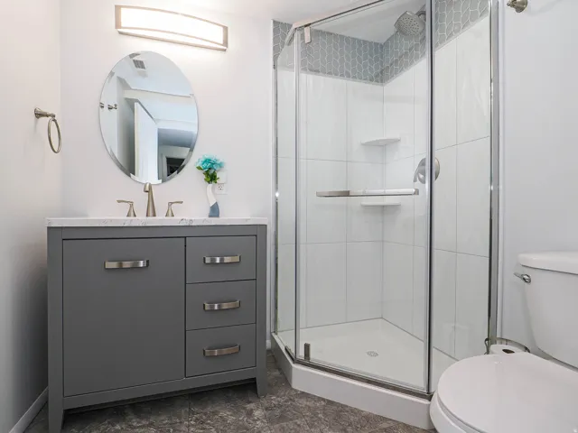Contemporary bathroom featuring a gray vanity with a light-colored countertop, an oval mirror, and a sleek rectangular light fixture