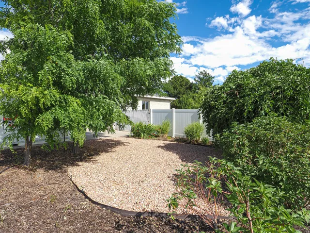 Gravel area surrounded by mature trees and shrubs, bordered by a white vinyl fence