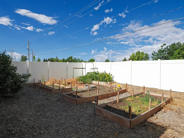 Private backyard featuring a white vinyl fence and multiple raised garden beds