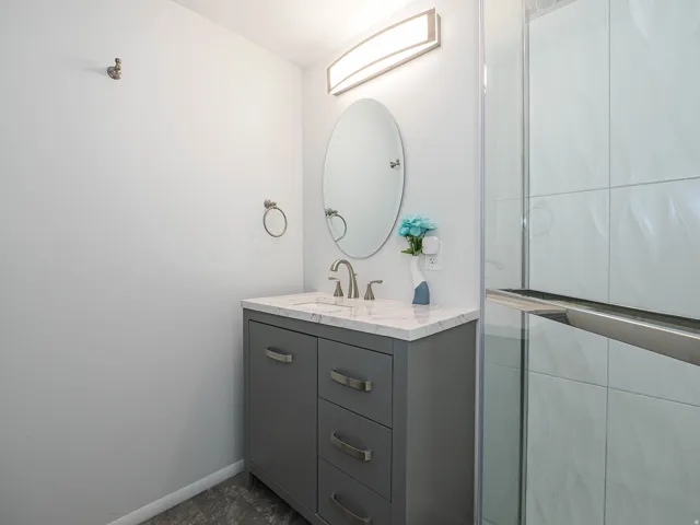 Contemporary bathroom vanity featuring a gray cabinet with brushed nickel hardware, a white countertop, and an oval mirror
