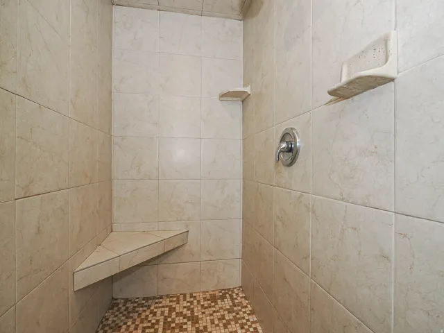 Tiled shower enclosure featuring a mosaic tile floor and a built-in corner bench
