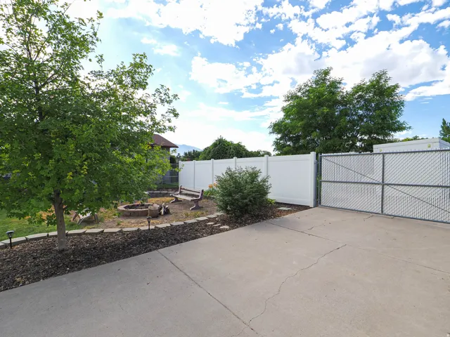 Concrete driveway with chain link gate, white privacy fencing, and a stone fire pit area