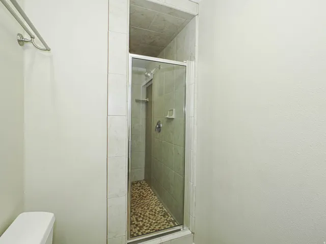 Tiled shower enclosure featuring a glass door, pebble-finish floor, and chrome fixtures