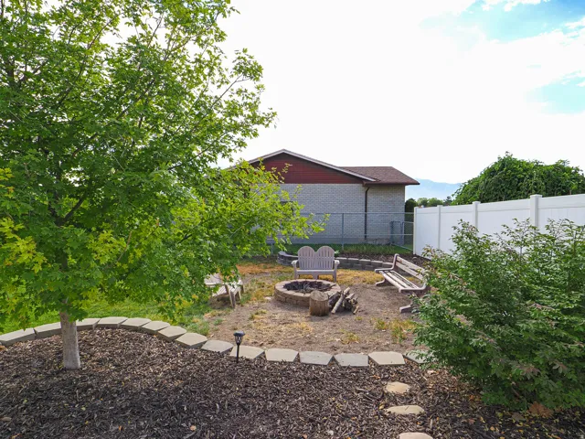 Backyard fire pit area featuring a stone-lined fire pit, surrounding wood benches, and a white vinyl privacy fence