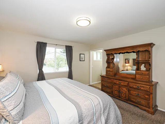 Carpeted bedroom featuring a flush-mount ceiling light fixture, a window with blinds, and a doorway leading to another room