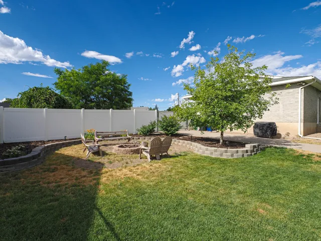 Backyard fire pit area with block retaining walls, surrounded by a white privacy fence and a brick-sided structure