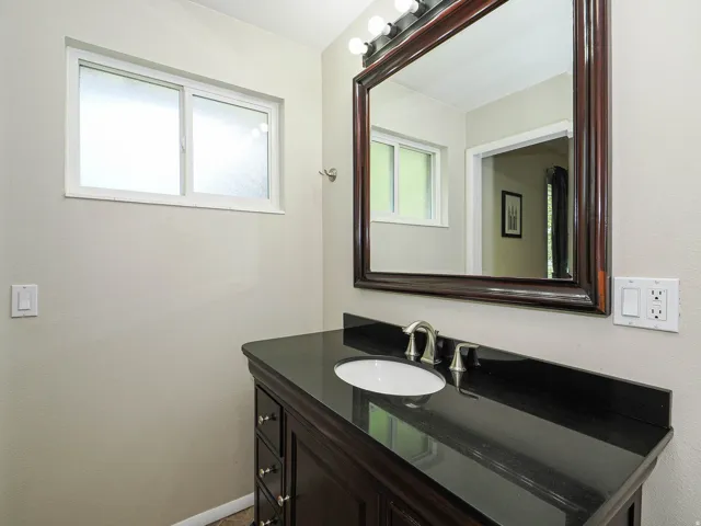 Dark wood-finish vanity with an undermount sink, brushed nickel faucet, and a black countertop