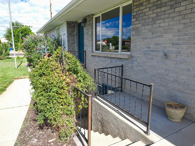 Gray brick exterior featuring a white fascia and soffit, a teal entry door, and a basement entry with wrought iron railings