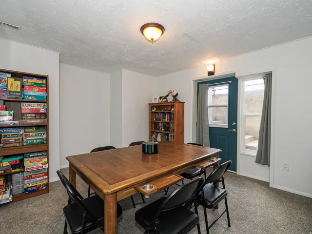 Carpeted room featuring a wooden table with built-in cupholders, recessed lighting, and a walk-out door with an adjacent window