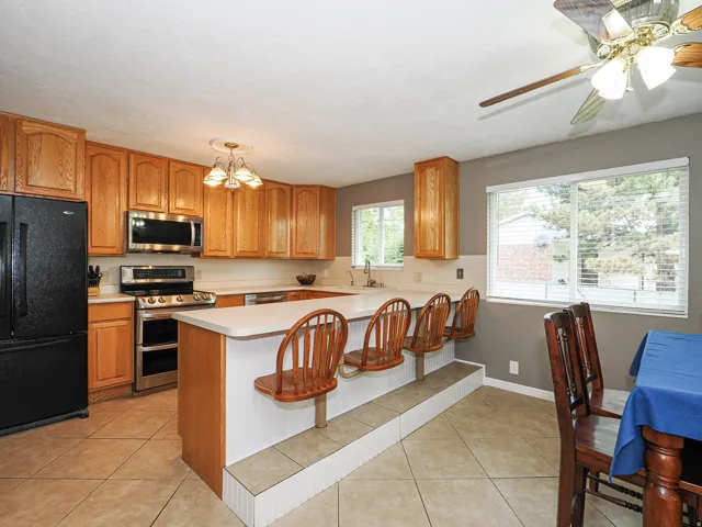 Kitchen featuring wood cabinetry, stainless steel appliances, a breakfast bar with built-in seating, tile flooring, and multiple windows