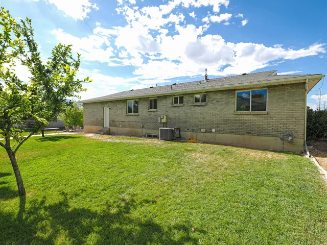 Spacious backyard featuring a lush lawn, mature shade tree, and brick exterior with multiple windows