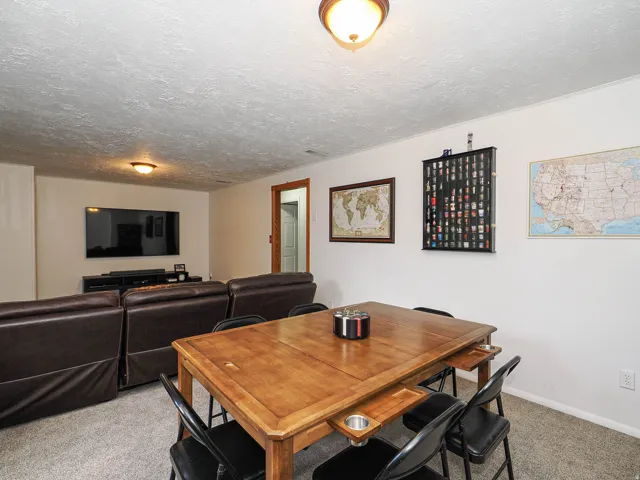 Carpeted interior space featuring a light wood-finish table, white walls, and a recessed ceiling light