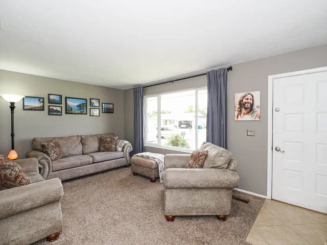 Spacious living area featuring neutral wall tones, textured carpeting, and a multi-pane window with drapery