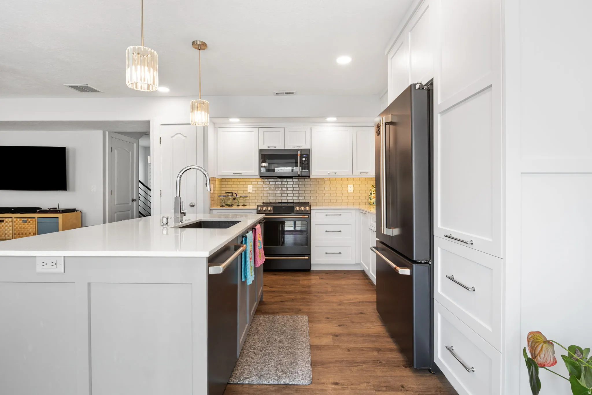 Kitchen featuring a spacious island with a sink, white cabinetry, a gold tile backsplash, and stainless steel appliances