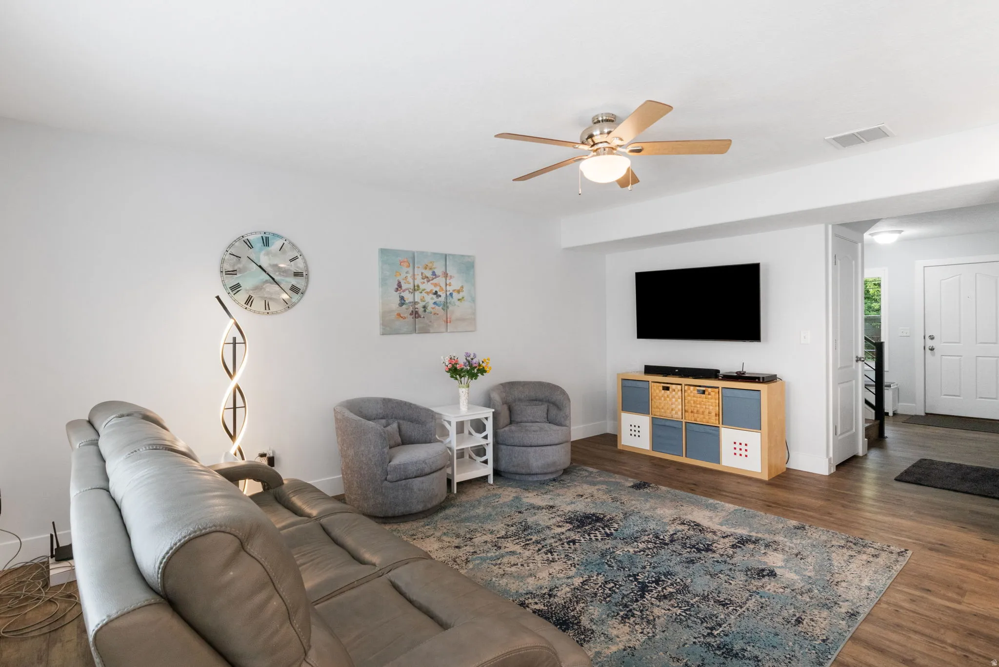 Living area featuring wood-finish flooring, a ceiling fan with integrated lighting, and a wall-mounted television