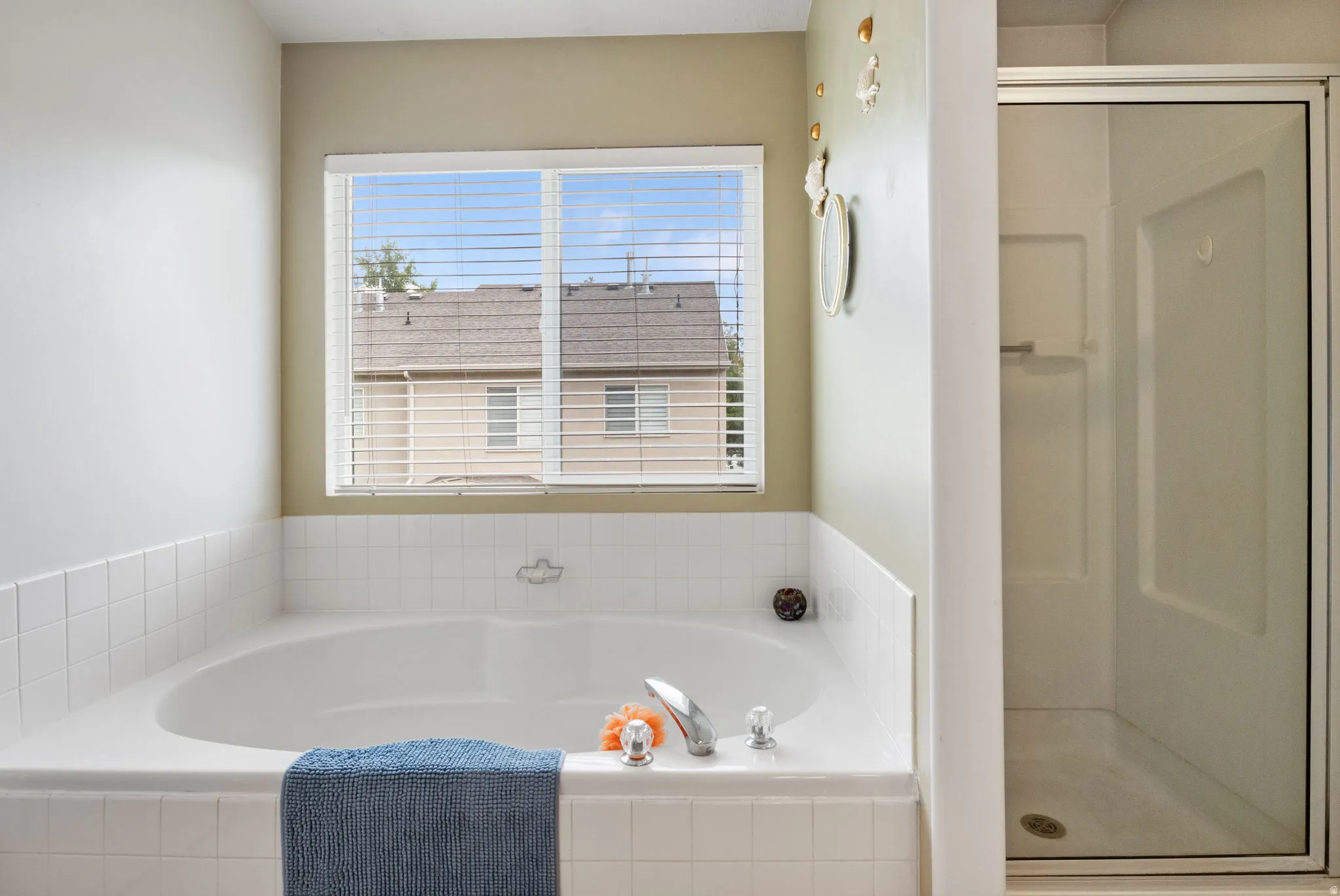 Soaking tub with white tile surround, privacy window with blinds, and chrome fixtures