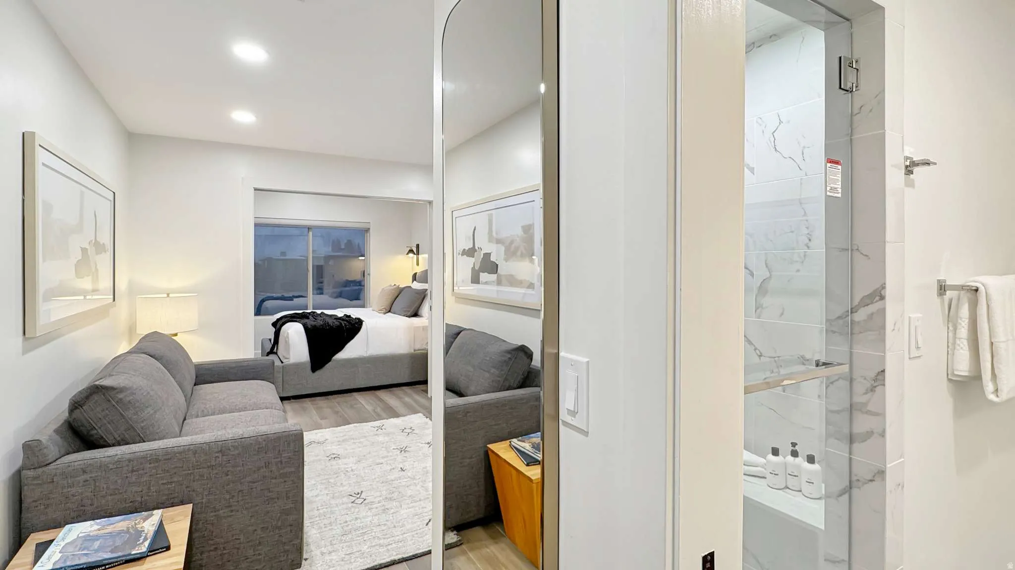 Open-concept living space with recessed lighting, wood-finish flooring, and a glass-enclosed shower featuring large format marbled tile