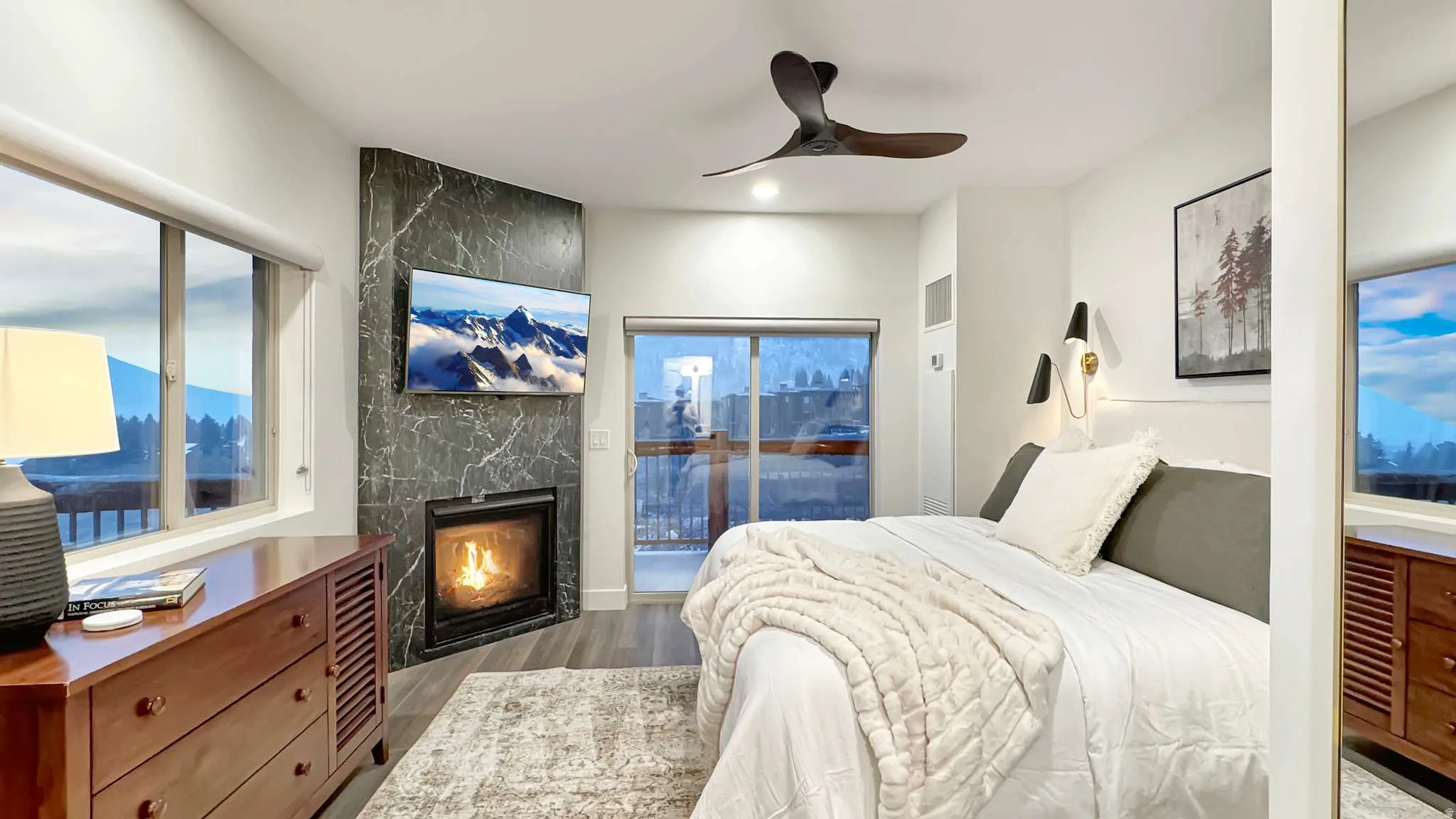 Corner fireplace with marble-look surround, mounted television, and a ceiling fan