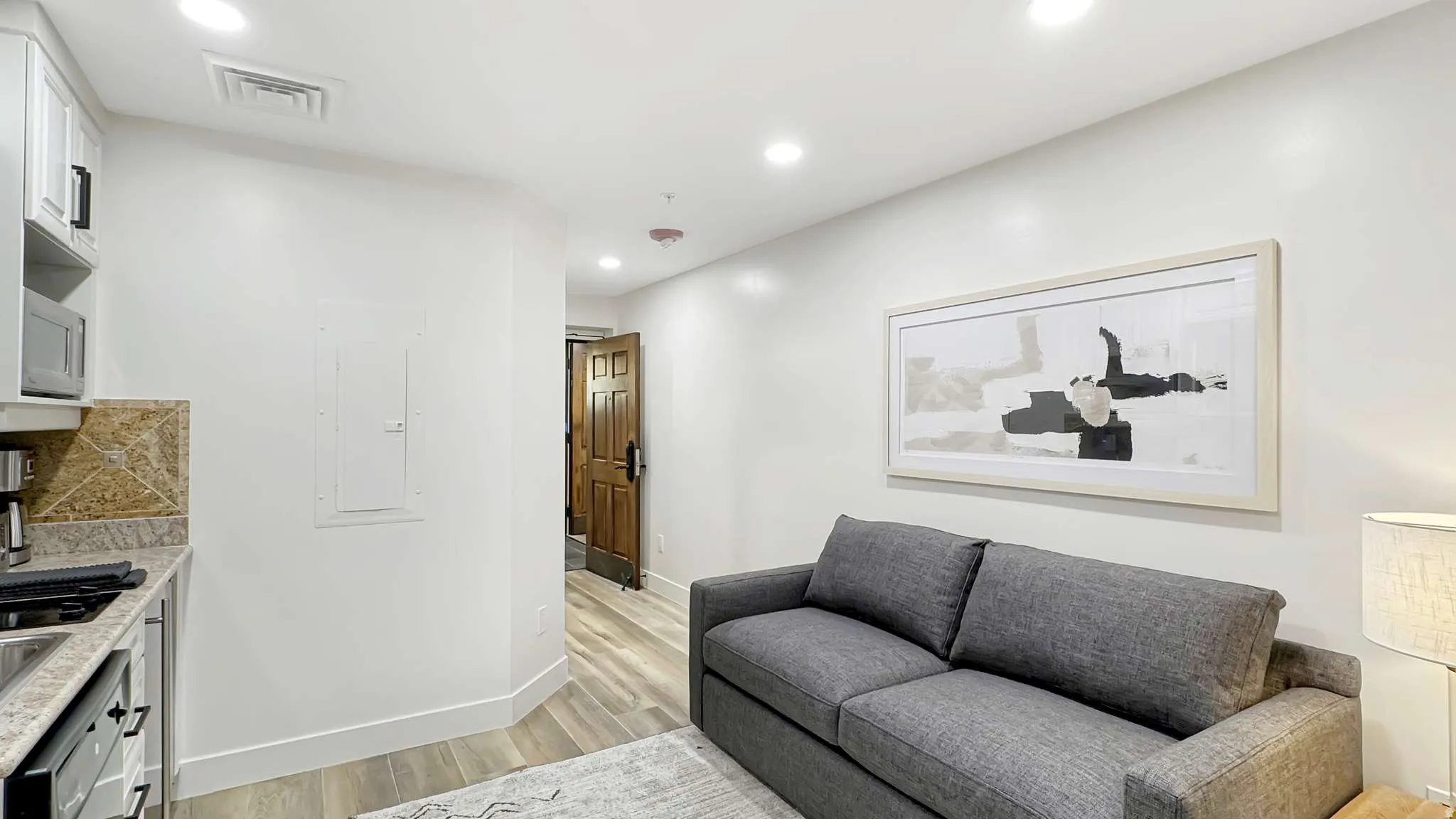 Compact living area featuring light wood-finish flooring, recessed lighting, and a partial kitchenette