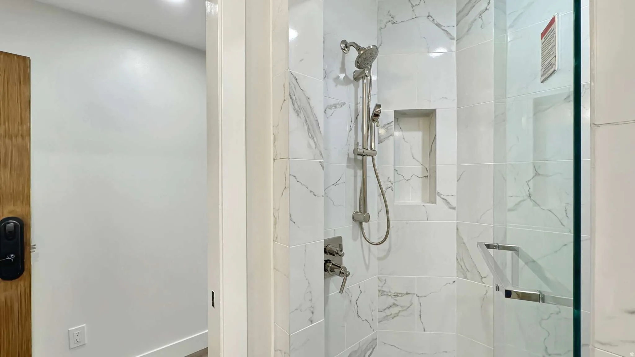 Shower enclosure featuring white marble-look tile, a built-in niche, and brushed nickel fixtures