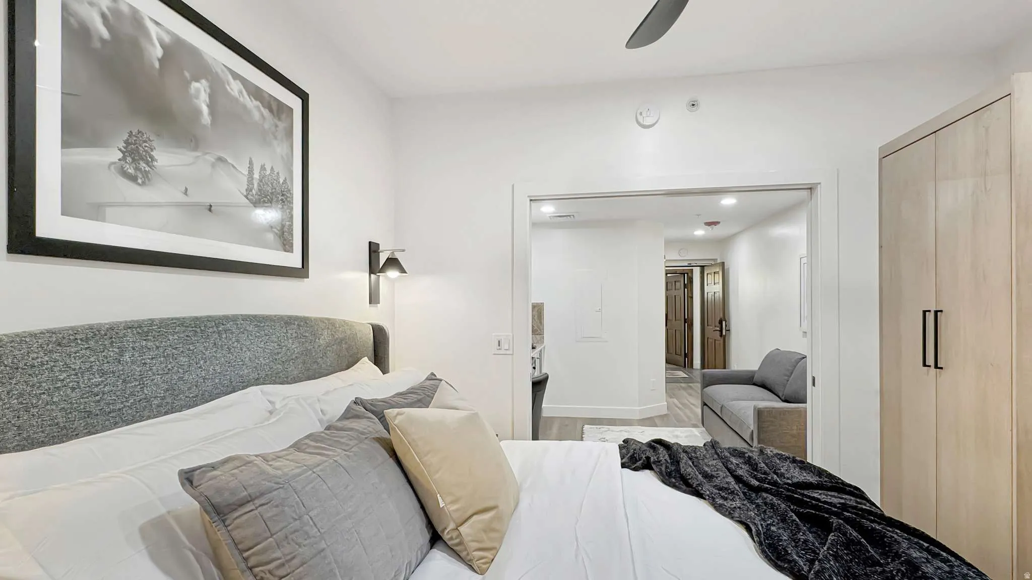 Bedroom with a fabric upholstered headboard, wall-mounted sconce lighting, and a light wood-finish built-in wardrobe