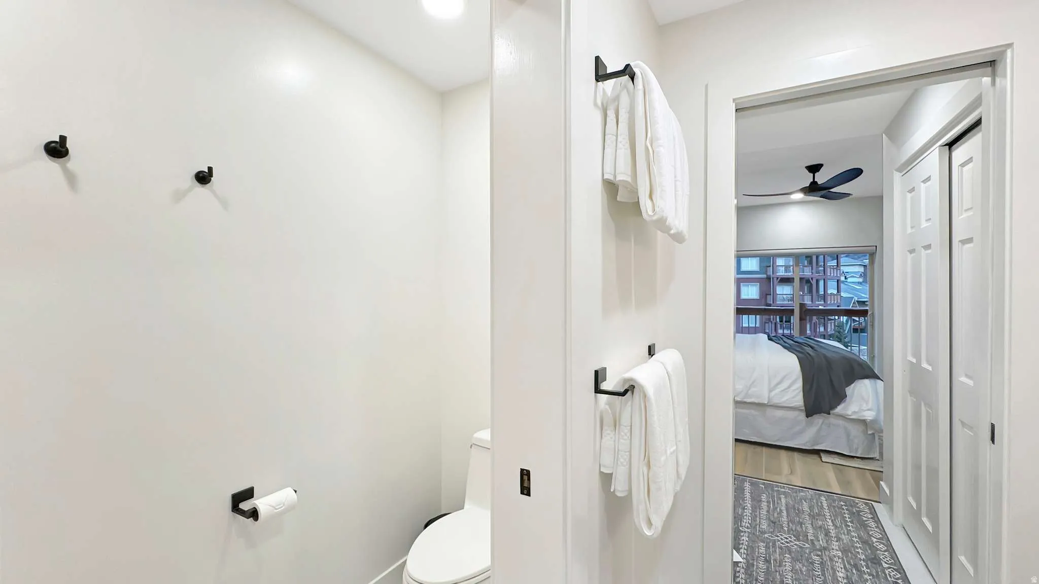 Recessed lighting illuminates a bathroom featuring a toilet with a white tank and bowl, and matte black hardware including towel bars, wall hooks, and a toilet paper holder