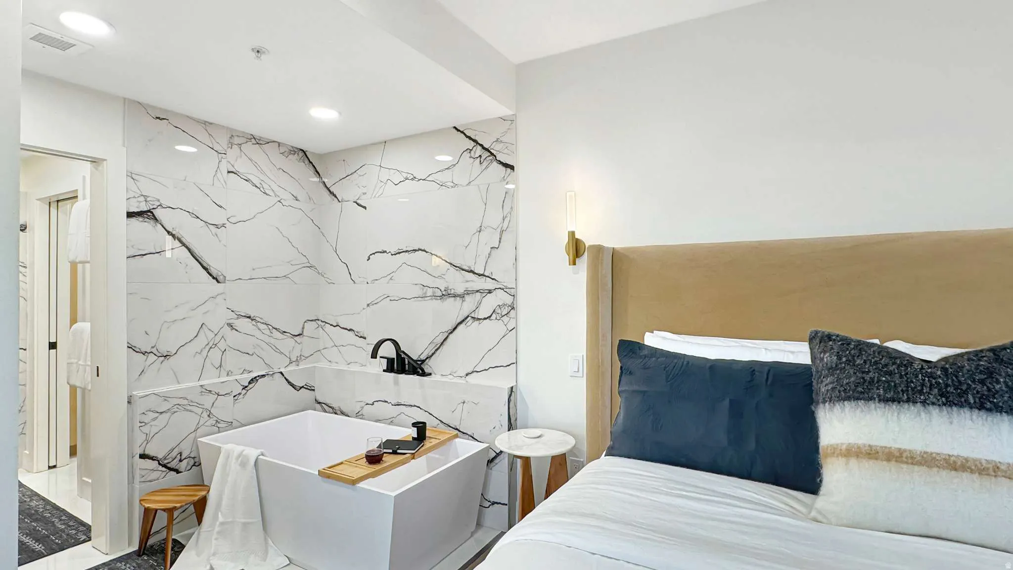 Freestanding square bathtub against a full-height wall of veined tile