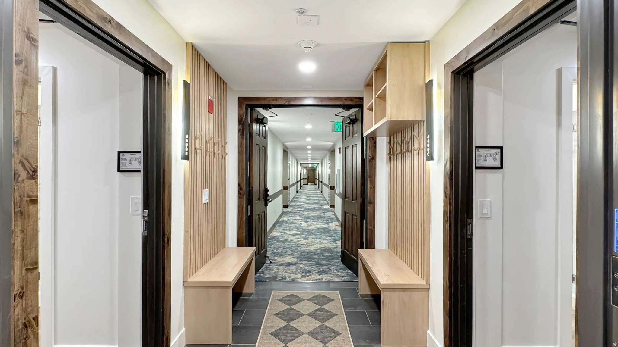 Hallway entry featuring custom built-in bench seating, vertical wood slat wall paneling, built-in shelving, dark wood trim, and wall-mounted sconce lighting