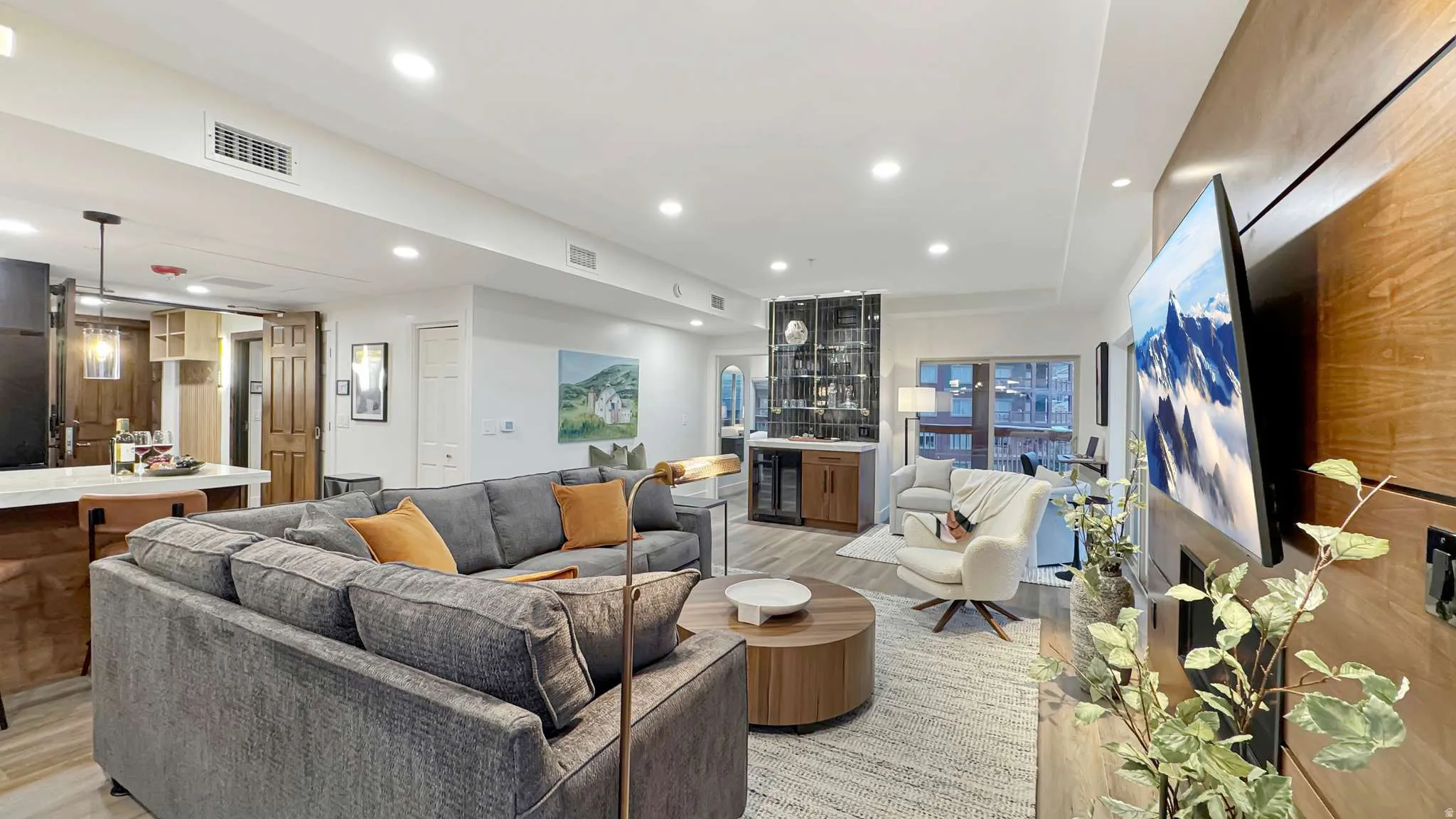 Open-concept living area featuring recessed lighting, wood-finish flooring, a built-in wet bar with glass cabinetry, and a large wood-paneled accent wall with built-in media integration