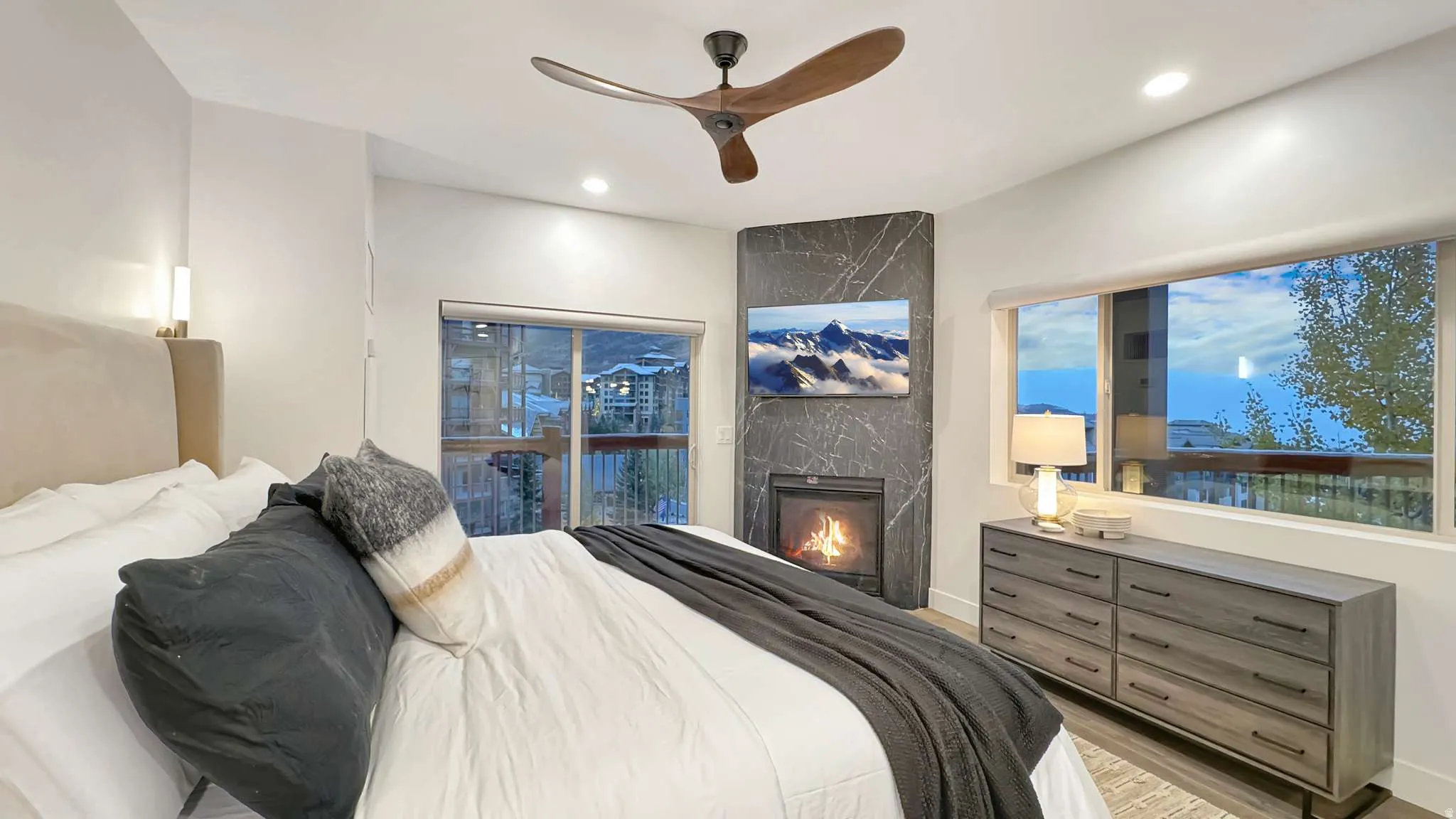 Recessed lighting illuminates this room featuring a ceiling fan with wood-finish blades, a built-in fireplace with a stone-finish surround, and a sliding glass door leading to a balcony