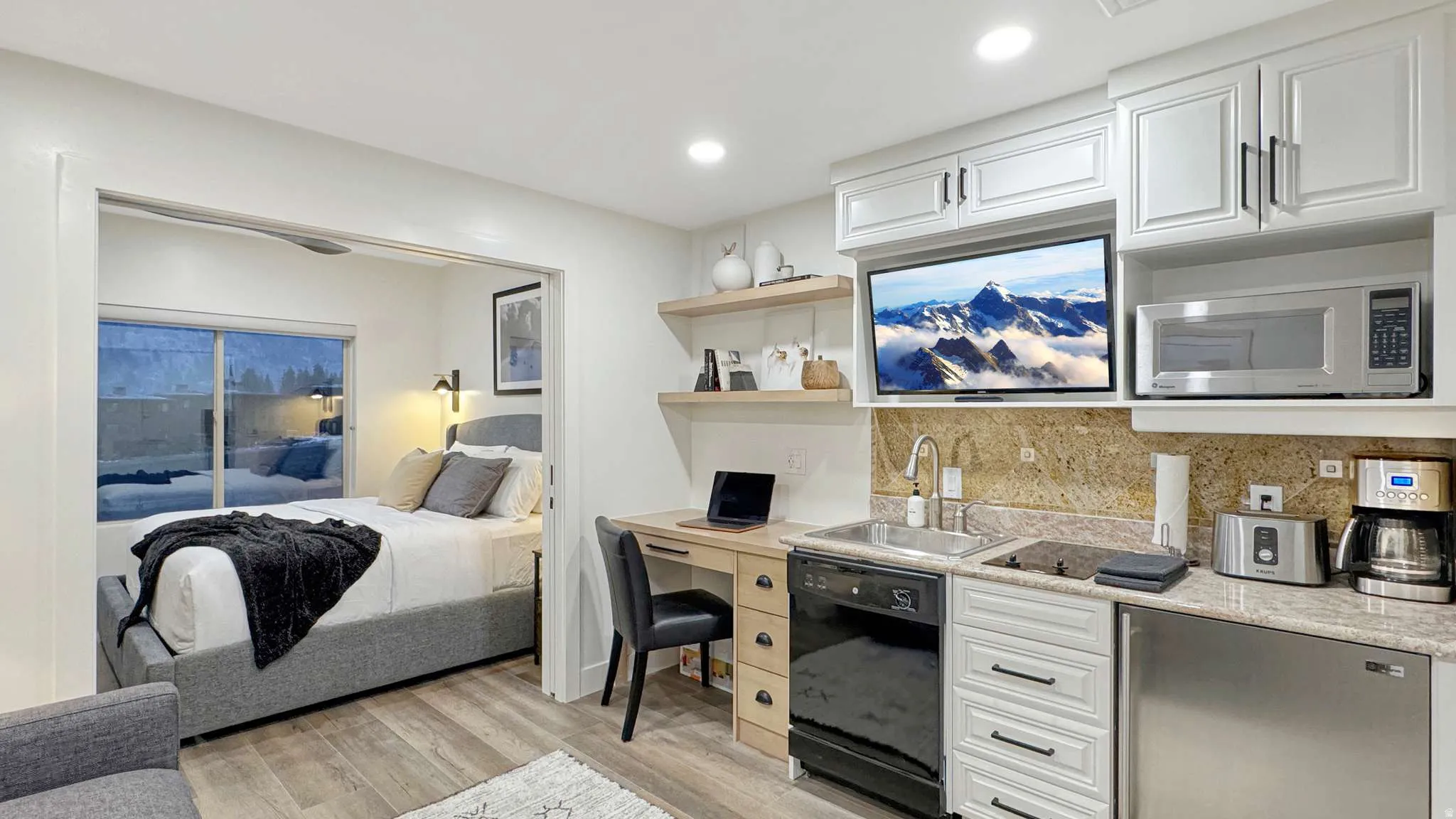 Compact kitchen area featuring white cabinetry, a built-in microwave, a stainless steel sink with a gooseneck faucet, and stone-finish countertops with a matching backsplash
