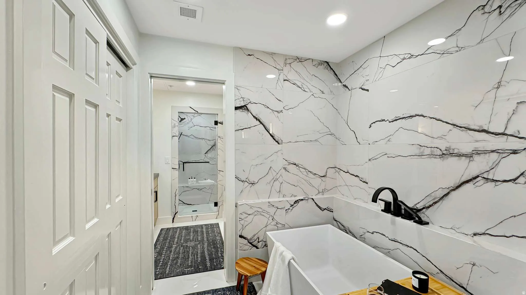 White tiled accent wall featuring black veining, freestanding soaking tub with matte black fixtures, and a glass-enclosed shower