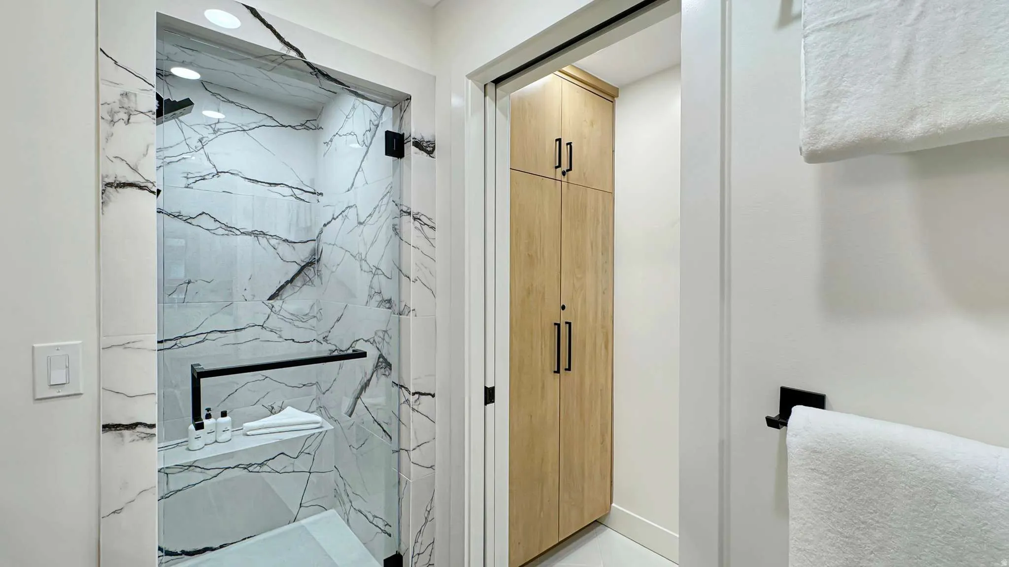 Glass-enclosed shower featuring large format white and black veined tiling, a built-in shower bench, and a rainfall showerhead