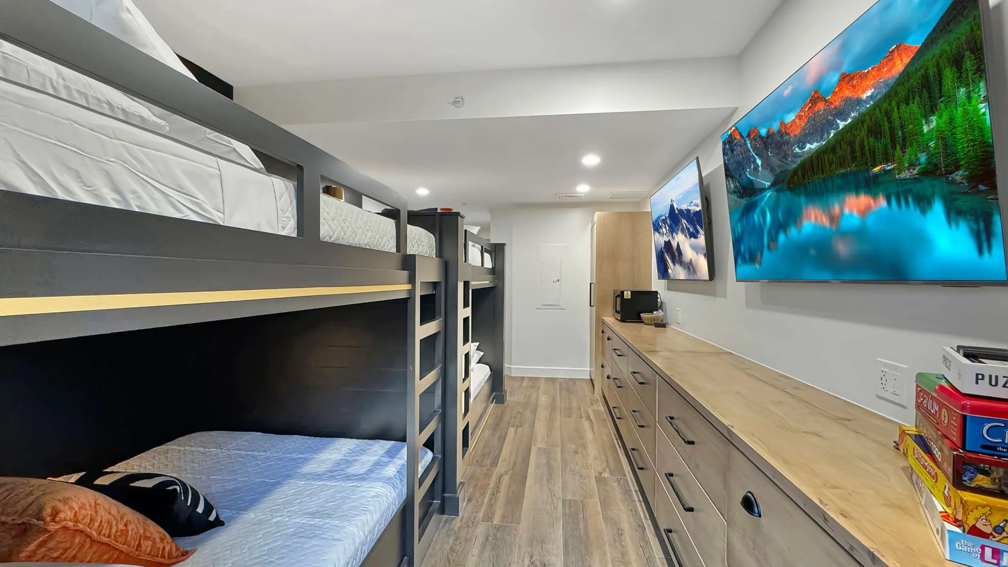 Bunk room featuring built-in bed frames, recessed lighting, wood-finish flooring, two wall-mounted televisions, and extensive built-in storage cabinetry with a wood-finish countertop