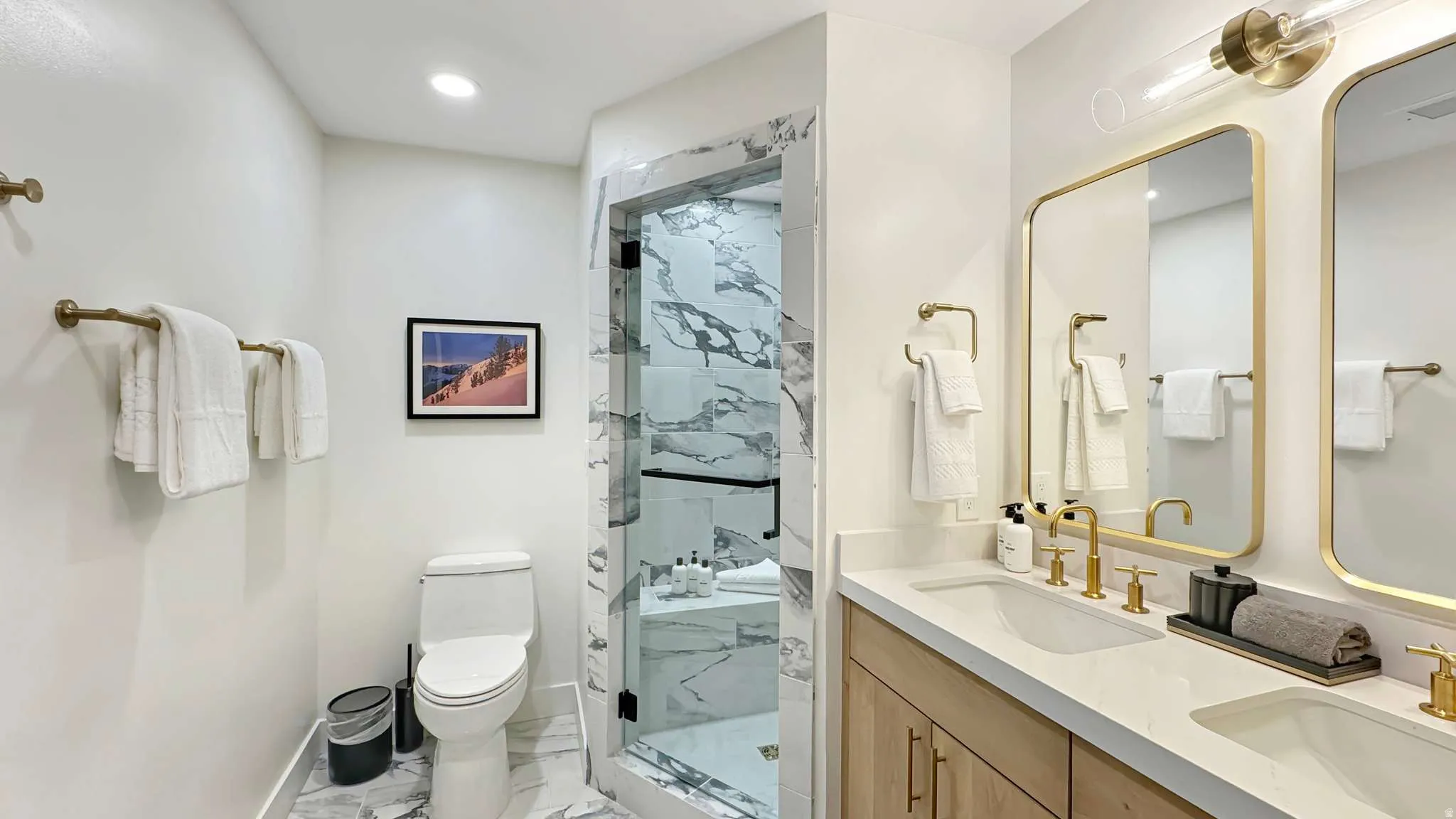 Contemporary bathroom featuring a double vanity with stone countertops and undermount sinks, gold-tone fixtures, and dual framed mirrors