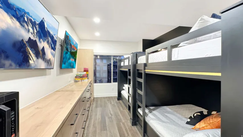 Room featuring multiple built-in bunk beds with black frames, wood-finish flooring, recessed ceiling lighting, and a window providing natural illumination