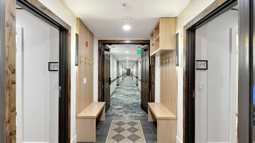 Hallway entry featuring custom built-in bench seating, vertical wood slat wall paneling, built-in shelving, dark wood trim, and wall-mounted sconce lighting