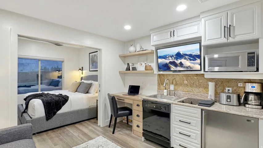 Compact kitchen area featuring white cabinetry, a built-in microwave, a stainless steel sink with a gooseneck faucet, and stone-finish countertops with a matching backsplash