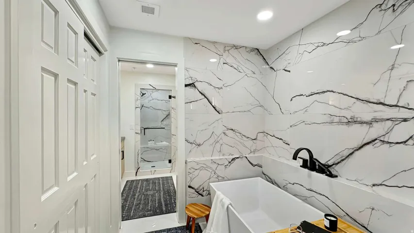 White tiled accent wall featuring black veining, freestanding soaking tub with matte black fixtures, and a glass-enclosed shower