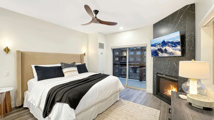 Bedroom featuring wood-finish flooring, a wall-mounted fireplace with a dark stone surround, and an overhead ceiling fan