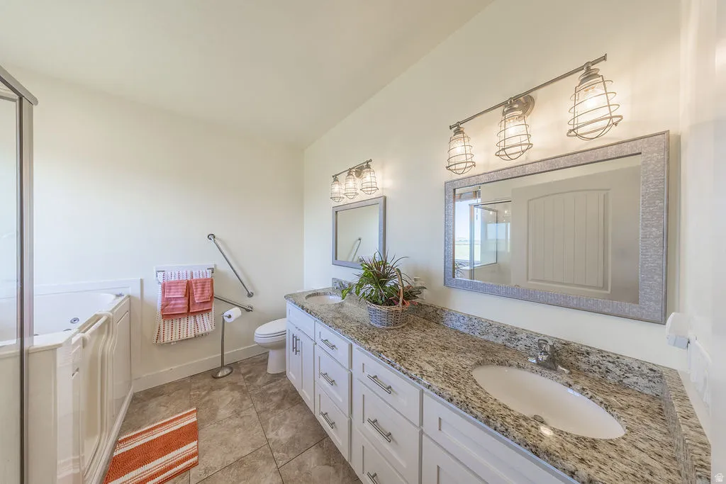 Spacious bathroom featuring a double vanity with stone countertops, a walk-in tub with glass enclosure, decorative light fixtures, and grab bars