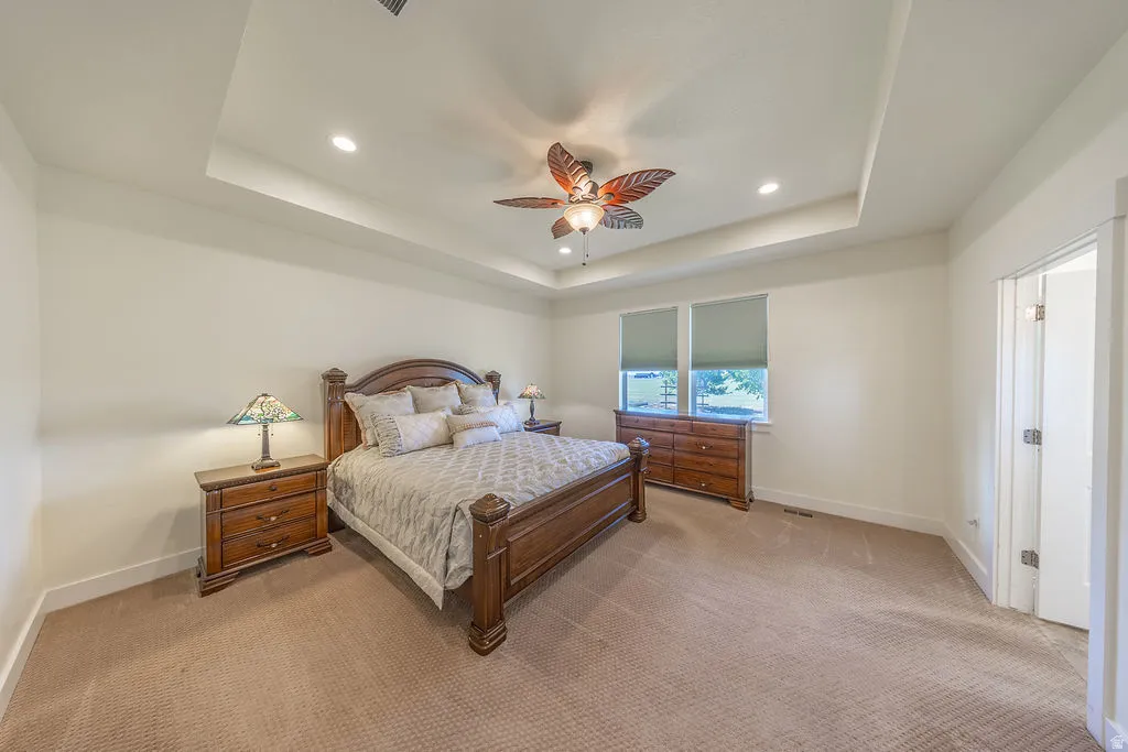 Primary bedroom with tray ceiling and windows with shades
