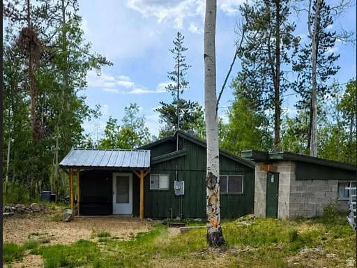 Wooded surroundings featuring a dark green exterior, covered porch entry with a metal roof, and a separate utility structure